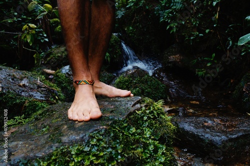 Feet without shoes and with indigenous bracelet on stone in the river