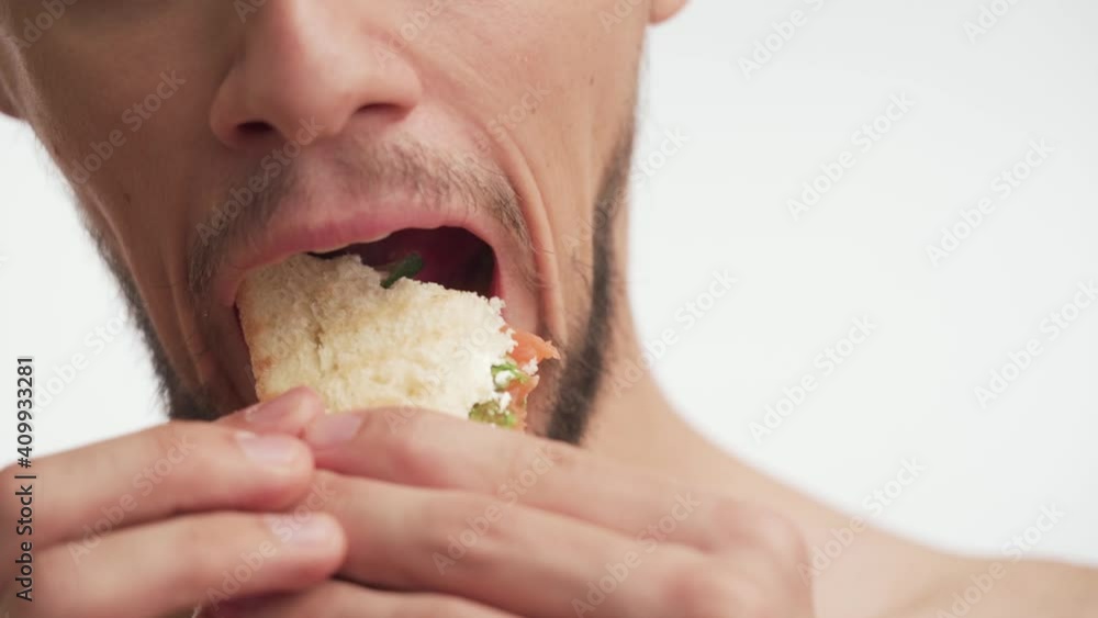 Close-up portrait of young 20s European handsome half naked brunette man with beard, moustache eagerly eat with pleasure fresh fish sandwich isolated on white background slow motion. Delicious food Close-up portrait of young 20s European handsome half naked brunette man with beard, moustache eagerly eat with pleasure fresh fish sandwich isolated on white background slow motion. Delicious food