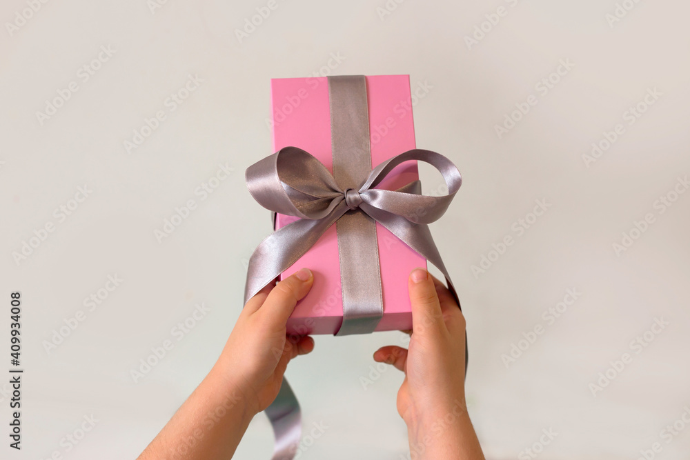child hands picking up a pink gift with silver ribbon child hands picking up a pink gift with silver ribbon