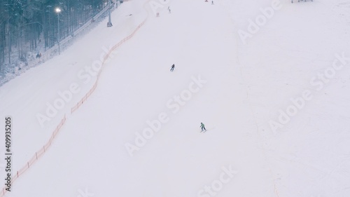 Aerial view of snowy skier snowboarder ride on a mountain track, ski slopes in the forested area in mountains. Top view of tracks near trees and ski resort in winter season.  4K 