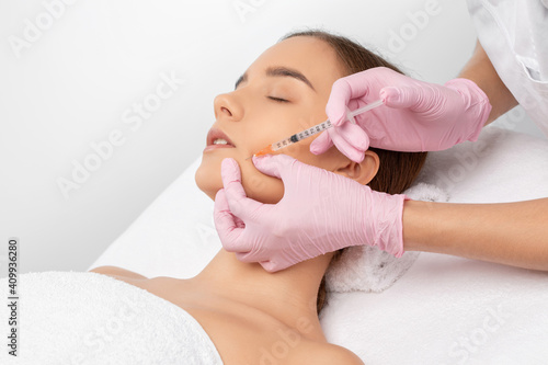 Cosmetologist makes rejuvenating anti wrinkle injections on the face of a beautiful woman. Female aesthetic cosmetology in a beauty salon.