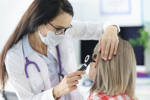 Otorhinolaryngologist examining patients sore ear with otoscope in clinic photo