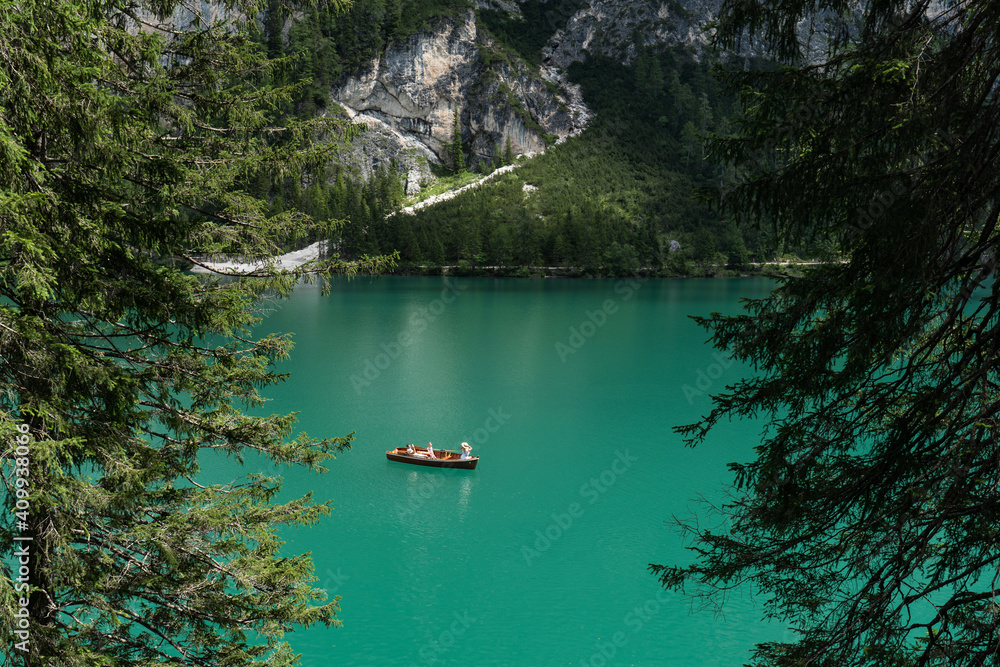 People on a boat, alone in Braies Lake. View between trees.