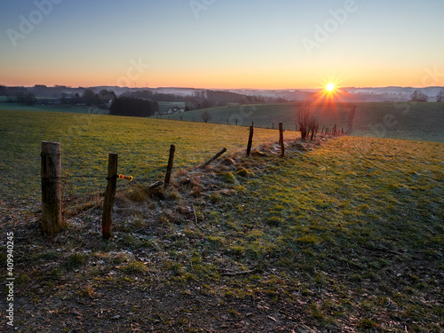 Frosty sunrise in the German city of Wipperfurth. A beautiful countryside landscape in the Bergisches Land region. Green pastures covered with frost in the rays of the rising sun.