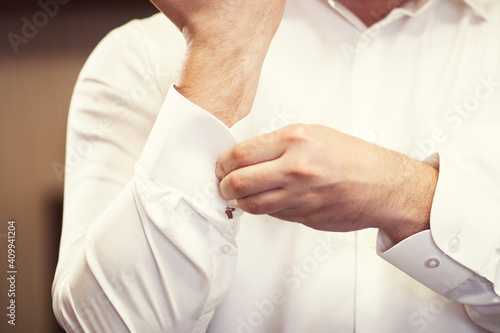 man fastens the cuffs on his white shirt. Close