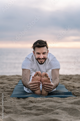 Happy Man with beard in white clothes doing stretching yoga exercises in the beach