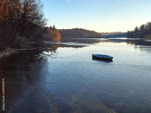 A lonely fishing boat on a partly frozen lake. Water reservoir at the Neyetalsperre dam in the German city of Wipperfurth. Water surface partially frozen. A frosty morning in the Bergisches Land.