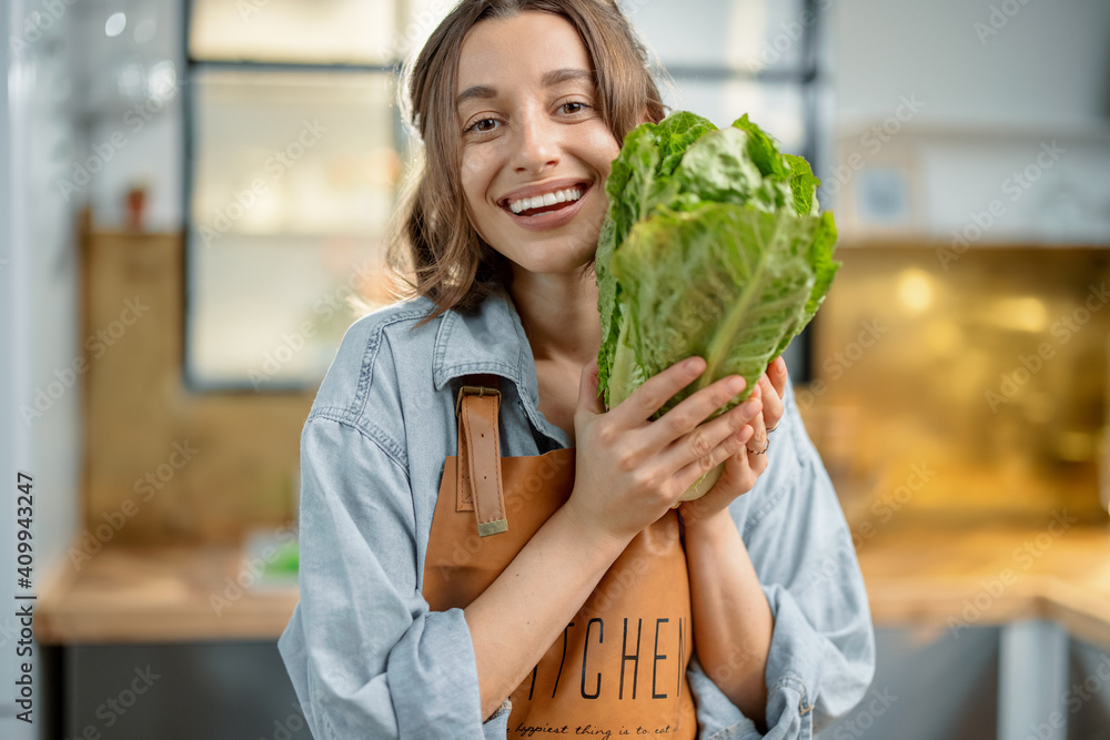 Portrait of pretty smiling woman in apron with fresh roman salad on the kitchen. Healthy cooking concept. Close up. High quality photo