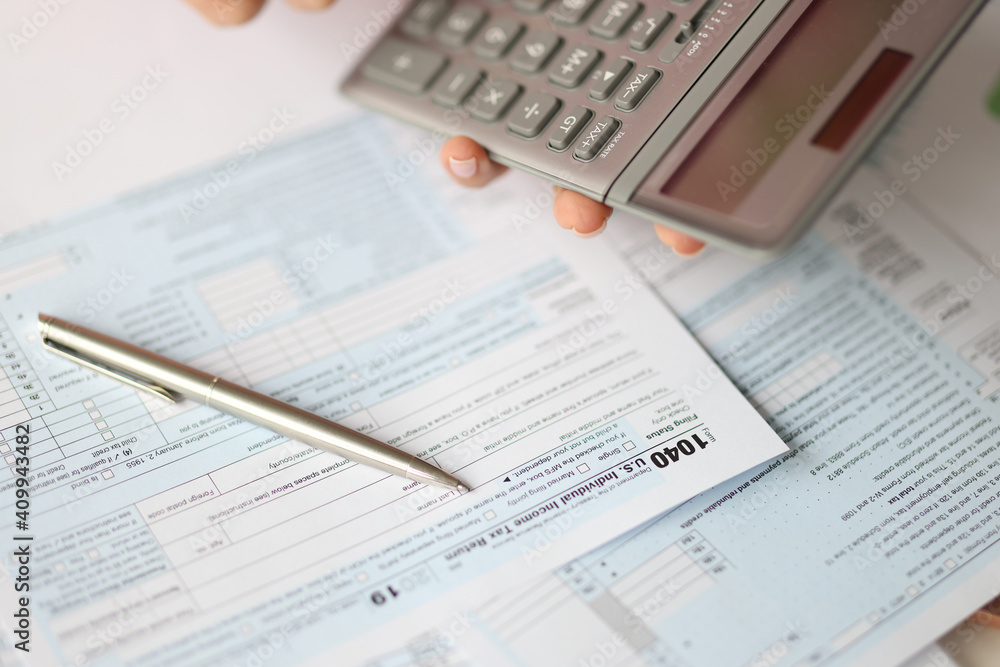 Hand holding calculator over tax form document closeup Hand holding calculator over tax form document closeup