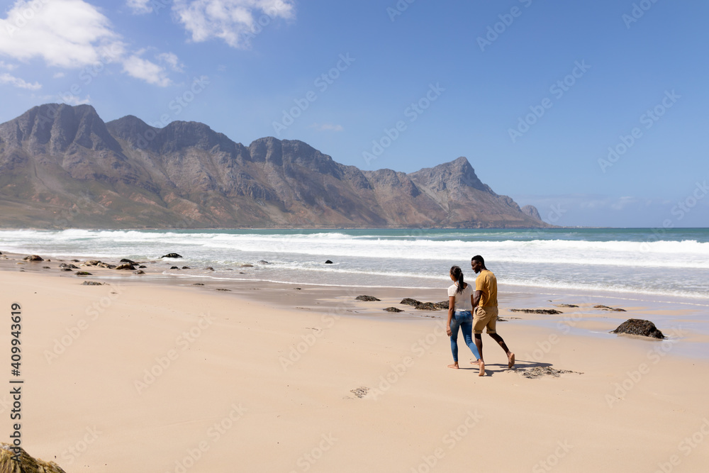 Naklejka premium African american couple walking holding hands on a beach by the sea