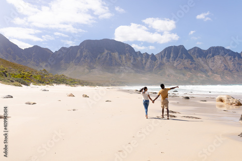 African american couple walking holding hands on a beach by the sea
