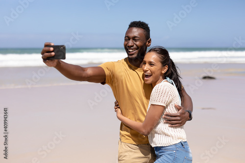 African american couple taking a selfie with smartphone on a beach by the sea