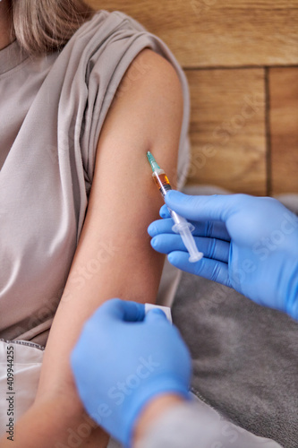 home doctor service. cropped doctor with syringe doing injection vaccine to young woman, flu,influenza in the shoulder of young woman, nurse injecting,vaccinating people. close-up photo