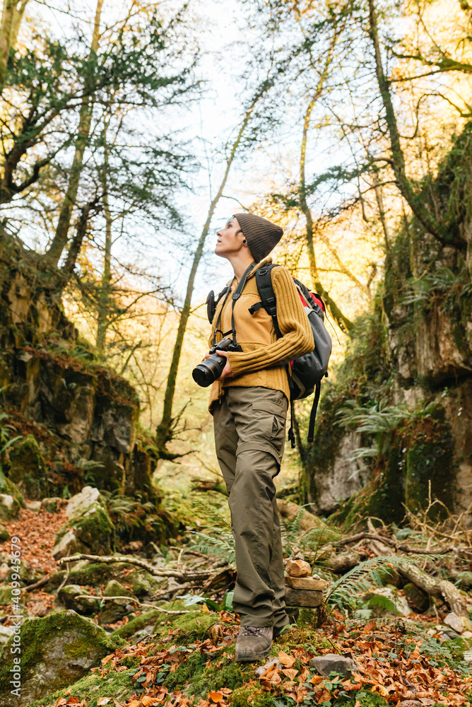 Low angle of traveling photographer standing in woods with photo camera and looking up while admiring nature during vacation Low angle of traveling photographer standing in woods with photo camera and looking up while admiring nature during vacation