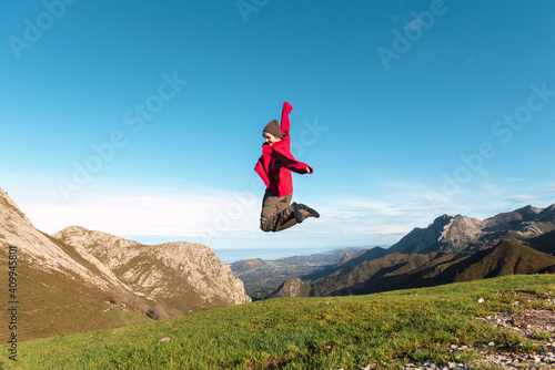 Side view of excited hiker jumping above ground in highlands and enjoying summer vacation in El Mazuco photo