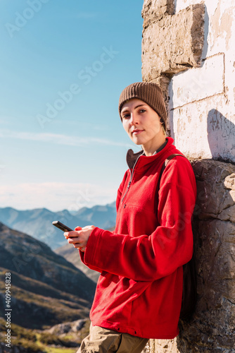 Side view of content hiker standing in highland area and browsing mobile phone while enjoying trekking in El Mazuco on sunny day looking at camera photo