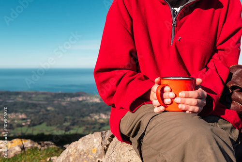 Unrecognizable crop explorer sitting on rock in highlands with metal mug of hot drink while relaxing during hiking in El Mazuco photo