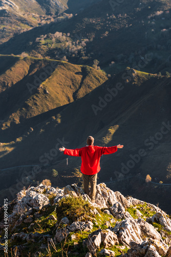 Back view of anonymous explorer standing with arms raised on green rock and admiring picturesque landscape of mountains in El Mazuco photo