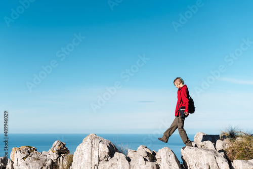 Side view of female hiker walking on rocks while trekking in highland terrain against blue sky in El Mazuco photo
