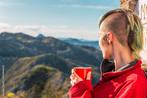 Side view of androgynous traveler standing in highlands on sunny day and enjoying hot drink during trip in El Mazuco looking away photo
