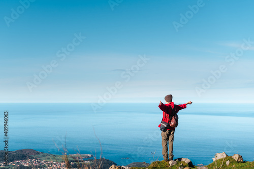 Back view of unrecognizable hiker standing with outstretched arms on edge of cliff and enjoying freedom during adventure in El Mazuco photo
