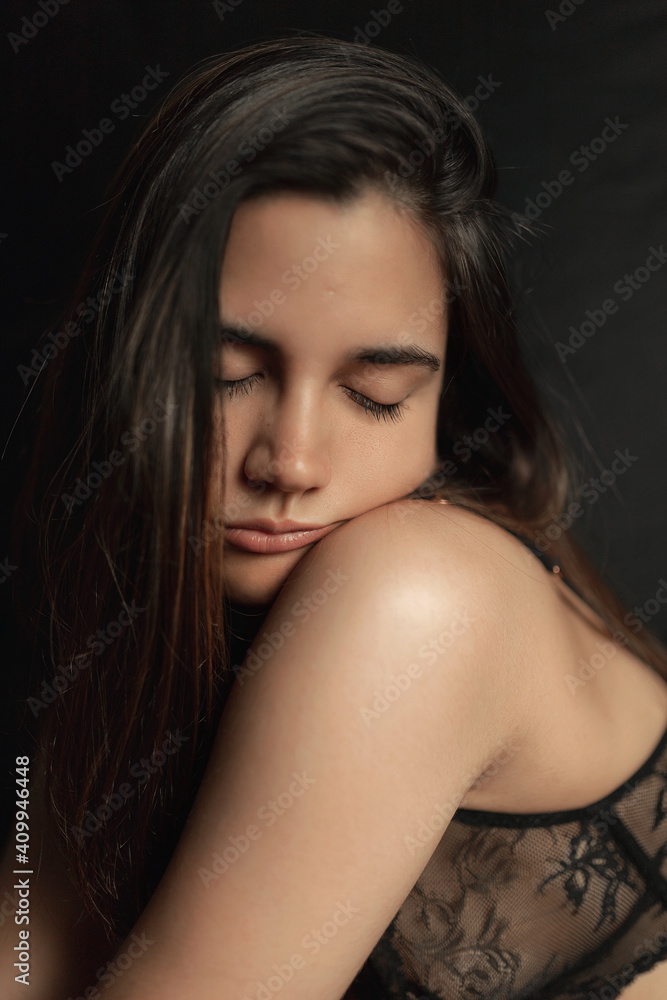 Serene slim female in black lace bra with eyes closed on dark background in studio Serene slim female in black lace bra with eyes closed on dark background in studio