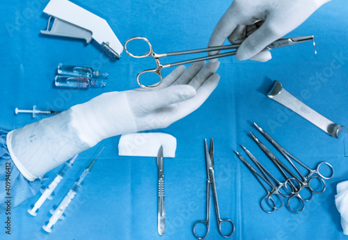 Top view of crop hand of anonymous assistant passing medical scissors to surgeon over table with various professional tools and instruments during operation in hospital photo