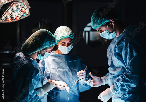 Group of focused professional surgeons with surgical tools and thread finishing operation of patient in operating theater photo