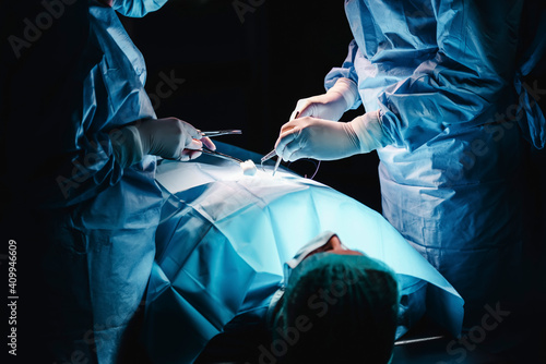 Crop anonymous surgeon and assistant with surgical tools and thread stitching wound of patient during operation in hospital photo