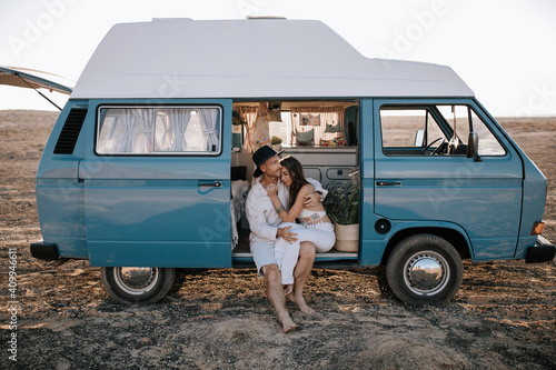 Loving couple of travelers sitting in parked van and hugging while spending summer vacation together photo