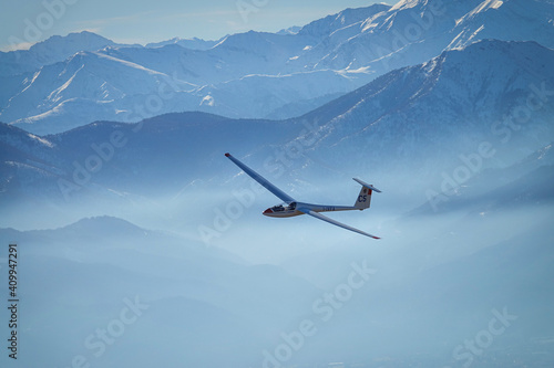 Glider in flight between snowy mountains seen from above. Susa, Italy - January 2021