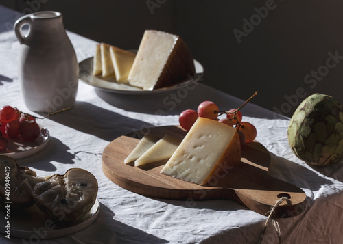 Ceramic jug placed on table with sweet fruits and delectable cheese in bright room lit by sunlight photo