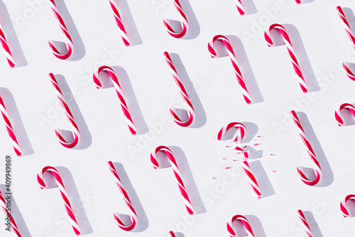 Top view full frame composition of red and white striped Xmas candy canes arranged in rows with one cane broken on white background