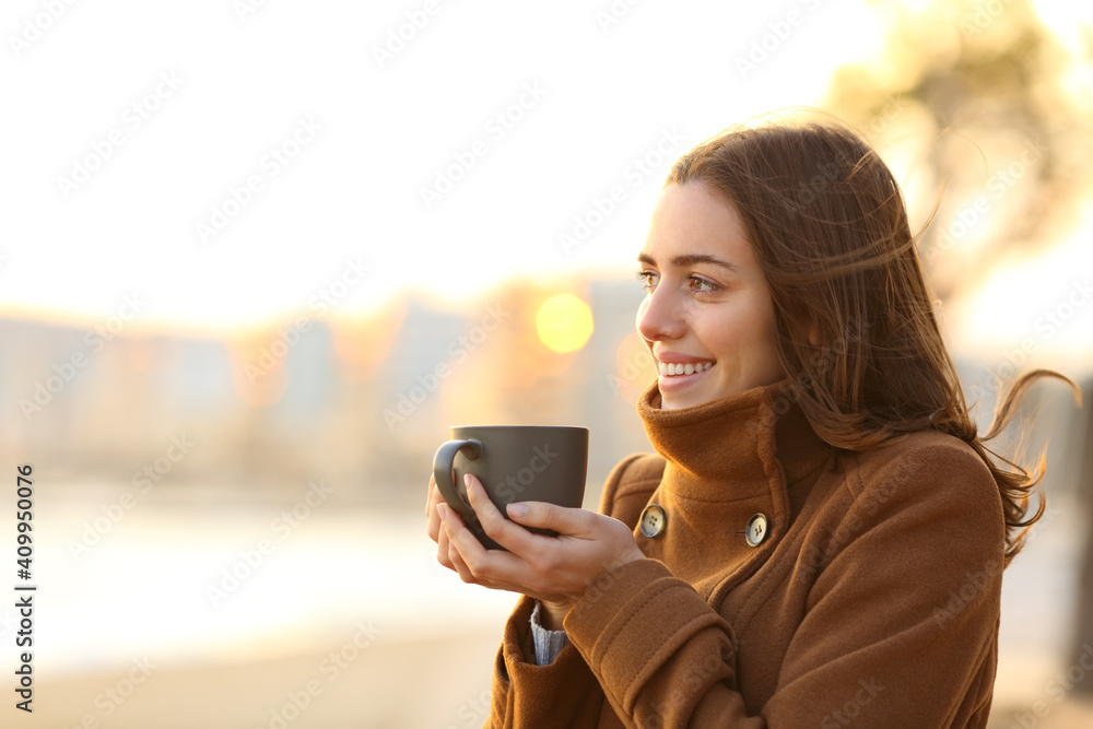 Happy woman drinks coffee in winter looking away on the beach Happy woman drinks coffee in winter looking away on the beach