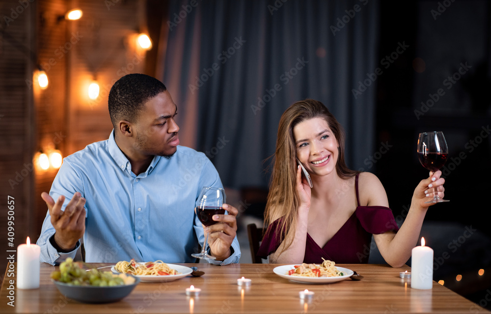 Woman talking on cellphone during romantic date, sitting next to angry boyfriend