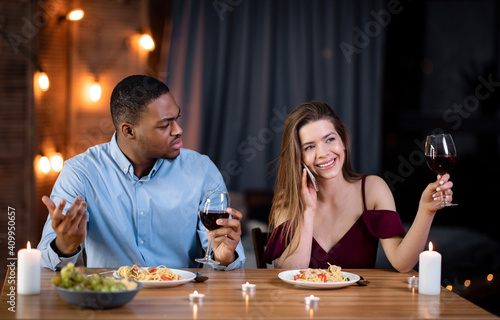Woman talking on cellphone during romantic date, sitting next to angry boyfriend