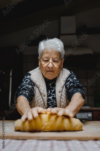 Senior female standing at table in cozy kitchen and kneading raw dough while preparing pastry for cooking domestic Italian tortellini photo