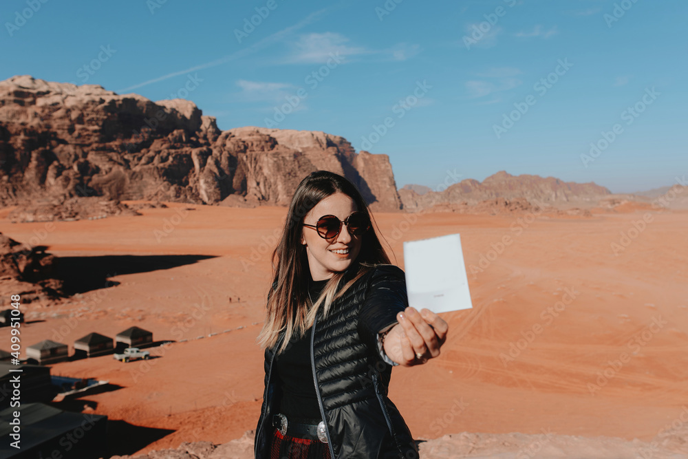 Smiling traveling female standing with old fashioned instant photo in Wadi Rum sandstone valley and looking at camera Smiling traveling female standing with old fashioned instant photo in Wadi Rum sandstone valley and looking at camera