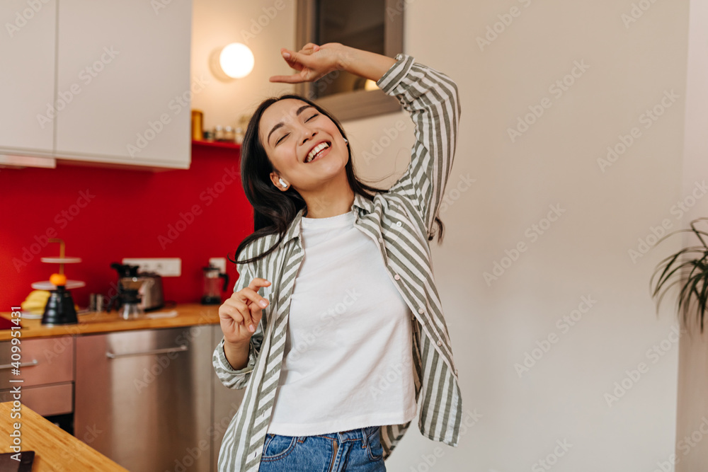 Joyful dark-haired woman dancing in kitchen and laughing