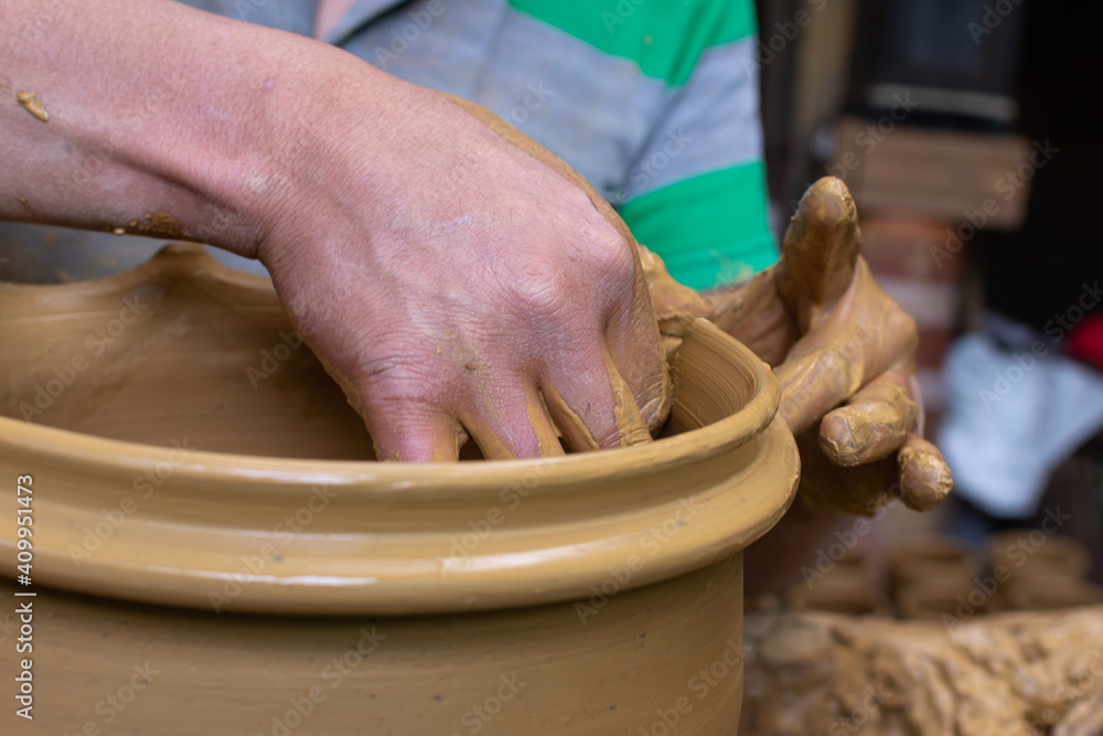 Wet and muddy hands of a craftsman shaping a clay vase on a pottery wheel. Artisan from Ráquira, Colombia. Shallow depth of field