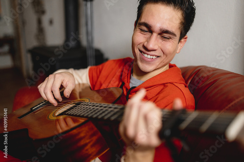 Close up young man portrait holding and playing the guitar. Concentrate and smiling guy enjoy the music. Hobby, relax, domestic life concept.