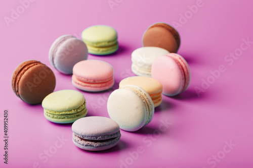 Colorful French macaroni cookies are scattered on a pink background.