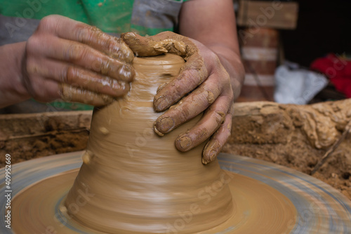 Wet and muddy hands of a craftsman shaping a clay vase on a pottery wheel. Artisan from Ráquira, Colombia. Shallow depth of field photo