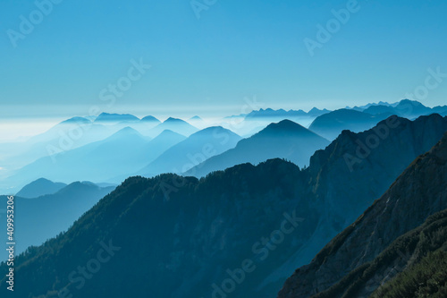 A close up view on the Alpine chains shrouded in the morning fog, seen from the top of Mittagskogel in Austria. Clear and sunny day. Sharp peaks around. Sun is shining above the high peaks. Serenity