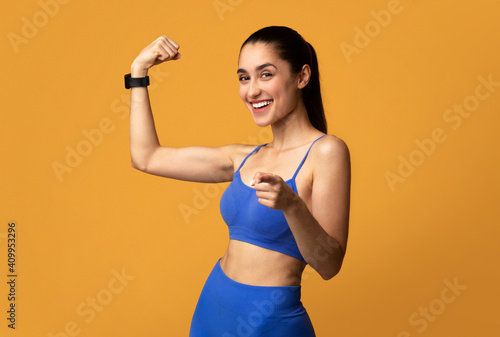 Happy sporty woman showing biceps and pointing to camera