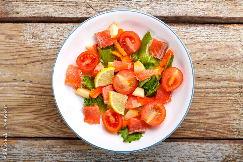 Salad with salmon and cherry tomatoes and green salad in a plate on a wooden table. Copy space Salad with salmon and cherry tomatoes and green salad in a plate on a wooden table. Copy space