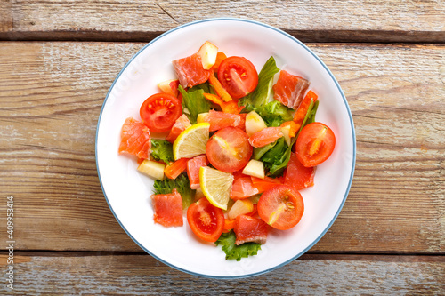 Salad with salmon and cherry tomatoes and green salad in a plate on a wooden table. Copy space