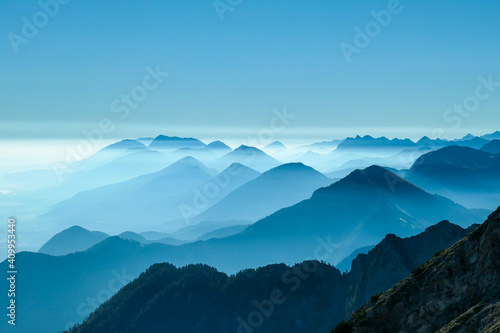 Fototapeta Naklejka Na Ścianę i Meble -  A close up view on the Alpine chains shrouded in the morning fog, seen from the top of Mittagskogel in Austria. Clear and sunny day. Sharp peaks around. Sun is shining above the high peaks. Serenity