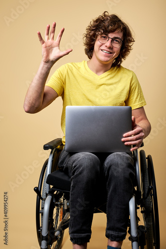 Принти на полотні handicapped male on wheelchair say hello at camera sitting on wheelchair with modern laptop, working online , smiling