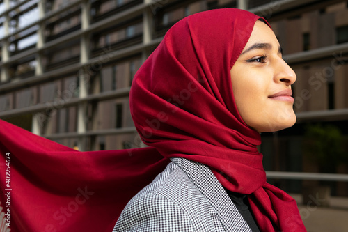 Side view of young content Arab female wearing red hijab standing on street and looking away photo